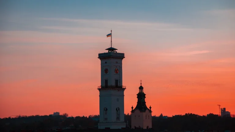 A tall, historic city hall clock tower silhouetted against a vibrant orange and pink sunset sky.