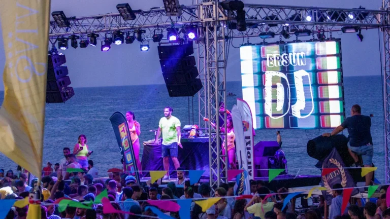 A live concert stage at Red Sun Buffet in Liepāja with 'SUN' visible on the LED screen and a crowd enjoying the music by the sea.
