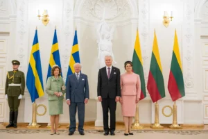 Four people in formal attire standing between Swedish and Lithuanian flags in an ornate hall.