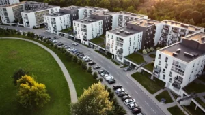 A high-angle view of a modern white apartment complex in Lithuania with green spaces and parking.