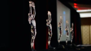 Clear crystal trophies shaped like human figures lined up on a dark stage under spotlighting.