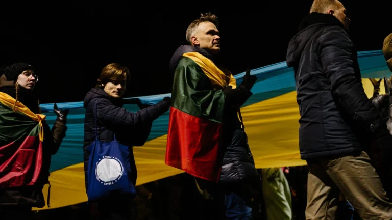 People in Lithuania carrying flags at a night rally, symbolizing public unity and support for national security.