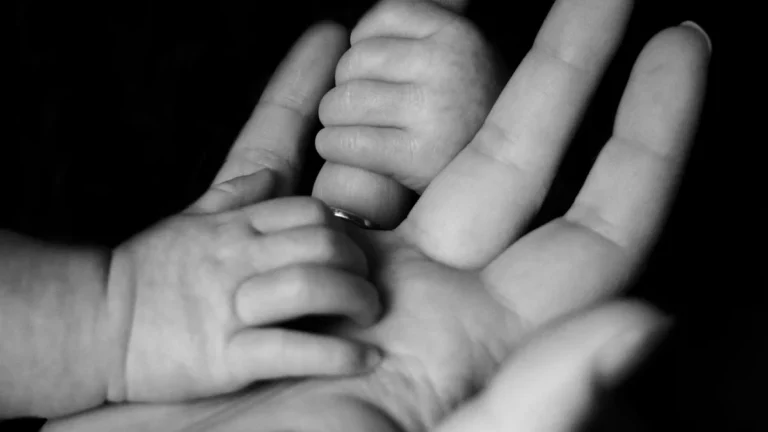 Black and white close-up of a newborn baby's small hands grasping an adult's fingers.