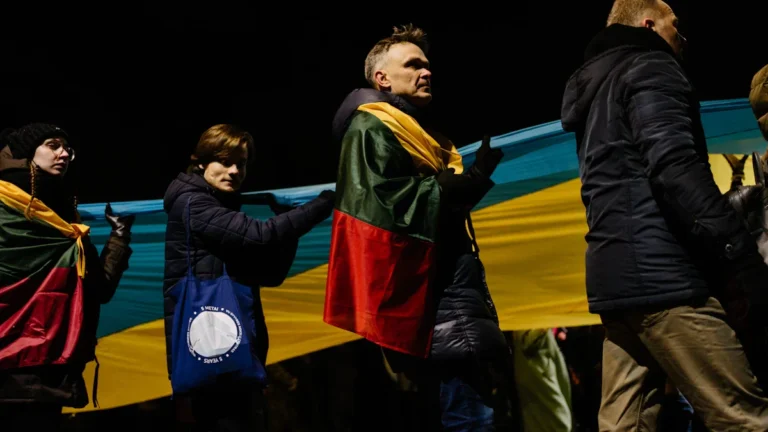 Protesters in Lithuania carry a large Ukrainian flag alongside the Lithuanian flag during a night demonstration.