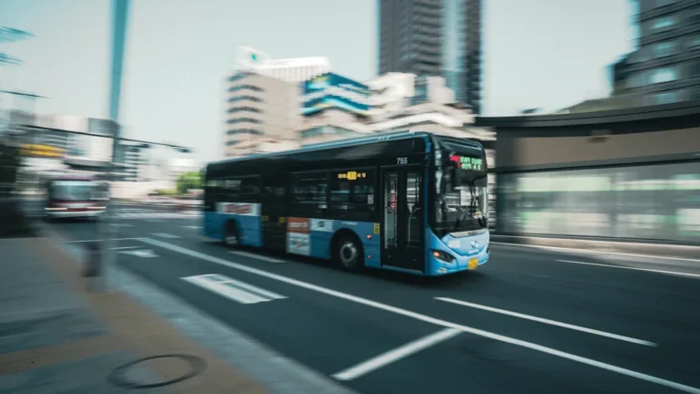 A modern blue city bus moving quickly through an urban intersection with dynamic motion blur.