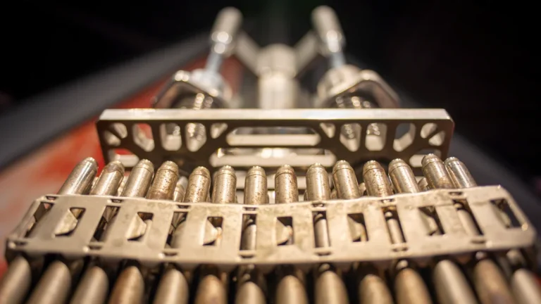 A close-up of a manufacturing machine at an arms factory processing a belt of high-caliber ammunition.