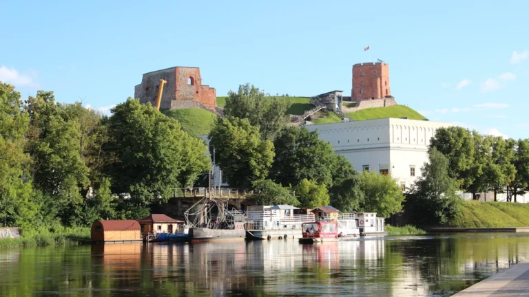 A scenic view of the Neris River in Vilnius, Lithuania, with historic buildings and Gediminas' Tower.