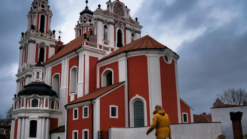 A pedestrian walks past the red and white facade of St. Catherine's Church in Vilnius.