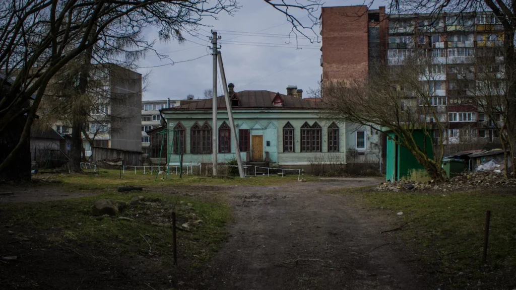 A traditional green house in Vilnius, Lithuania, contrasted against tall, grey Soviet-era apartment blocks.