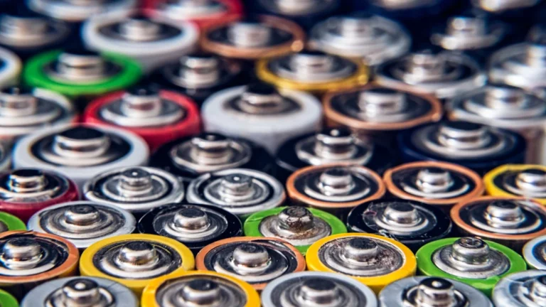 A dense collection of various used household batteries showing different sizes and colorful cases.