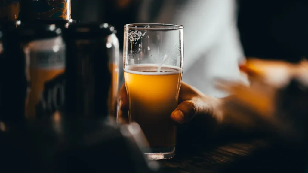 A close-up of a hand holding a glass of beer next to several cans in a pub.