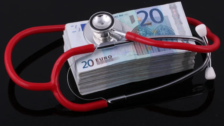 A red stethoscope resting on a thick stack of twenty Euro banknotes against a dark background.