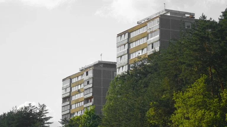 Multi-story residential apartment buildings in Vilnius, Lithuania, surrounded by green trees under a bright sky.