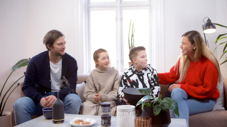A family of four sitting together in a modern, sunlit living room representing contemporary household support.