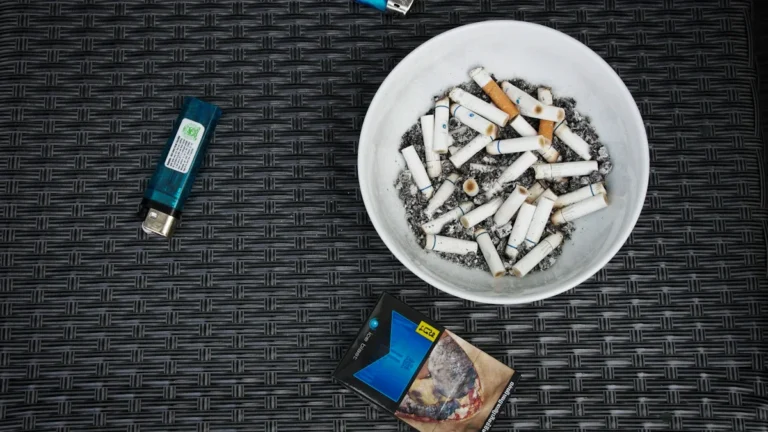 A pack of cigarettes with a graphic health warning lying next to a bowl of cigarette butts.