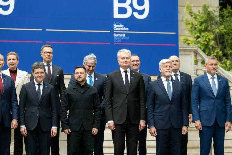 Leaders in suits stand for a group photo before a large blue Bucharest Summit banner.