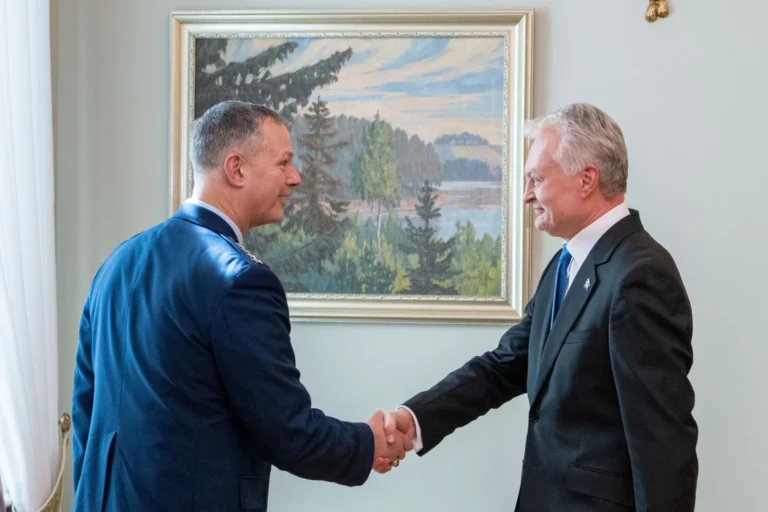 A military officer in blue uniform shakes hands with a man in a black suit.