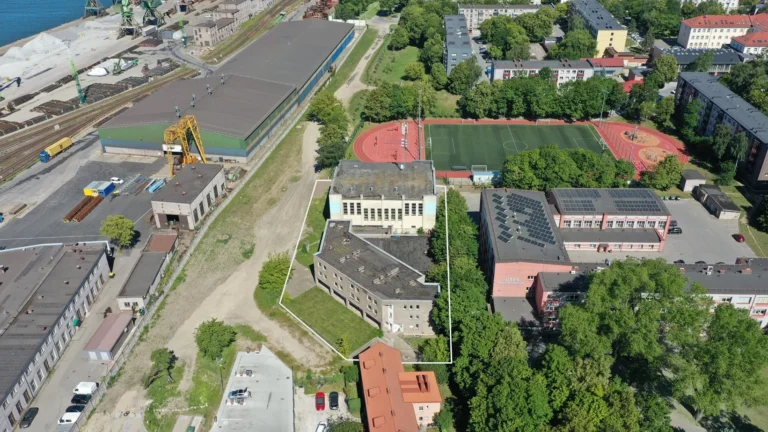 High-angle aerial view of a gray building outlined in white near a school and athletic field.