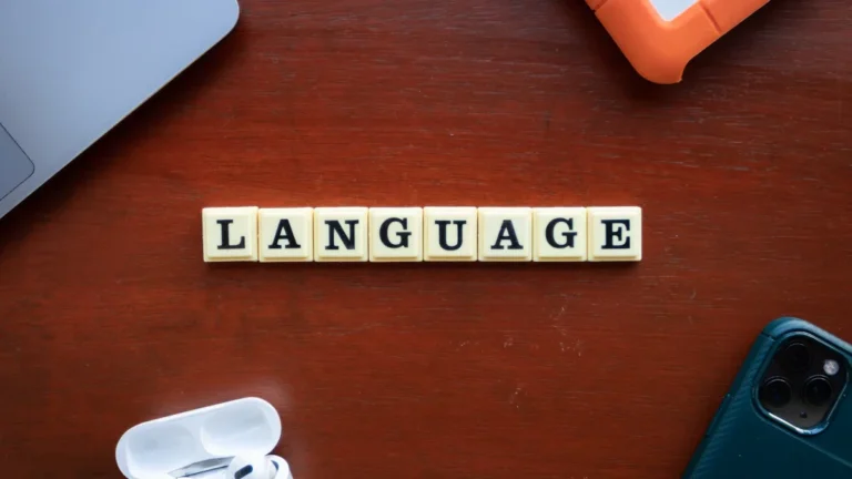 Scrabble tiles spelling the word 'LANGUAGE' centered on a dark wooden desk with electronic accessories.