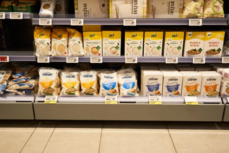 Assorted rice packages in bags and boxes arranged on supermarket shelves with visible price tags.