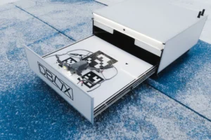 A small drone sits on a patterned landing pad inside an open white automated docking station.