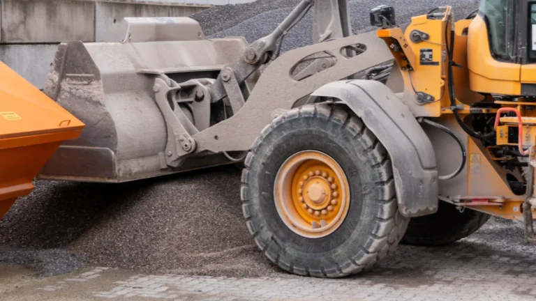 A large yellow loader scooping gravel into a truck at a European construction site.