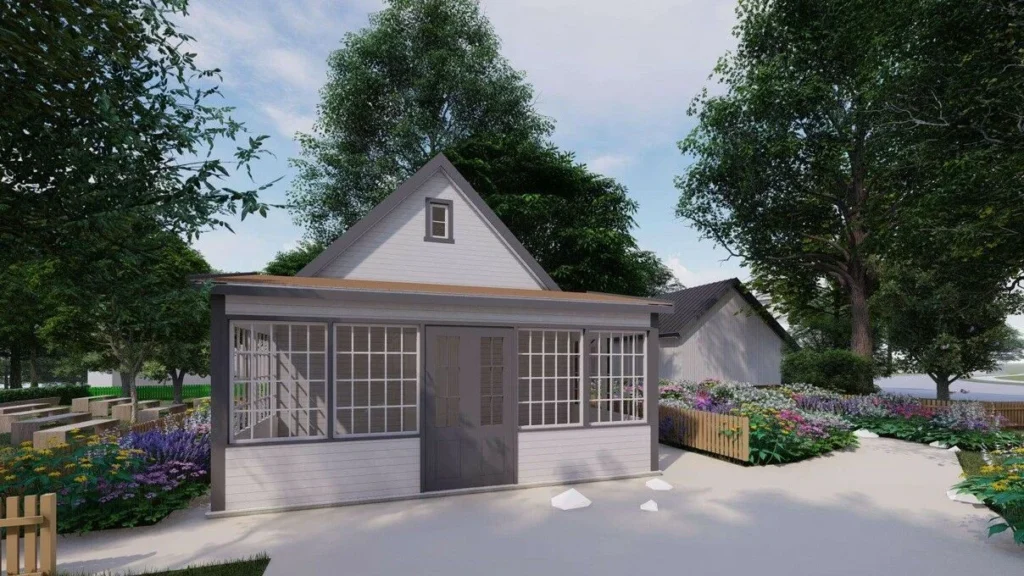 White gabled building with large windows and grey doors, surrounded by colorful flower beds and trees.