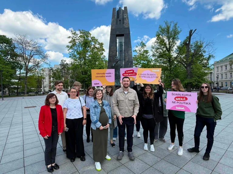 People holding pink and yellow signs in front of a large monument in a public square.