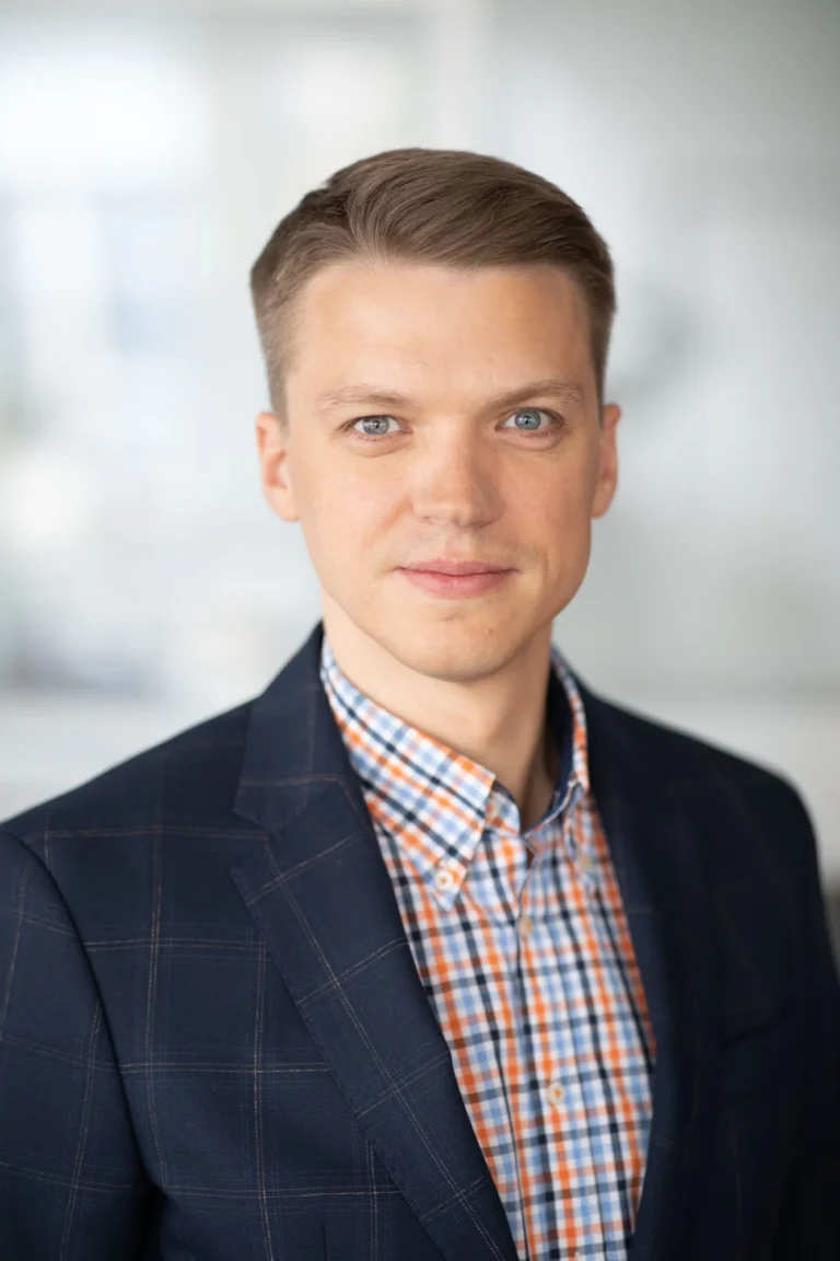 Professional headshot of a man with light brown hair wearing a blue plaid suit jacket.