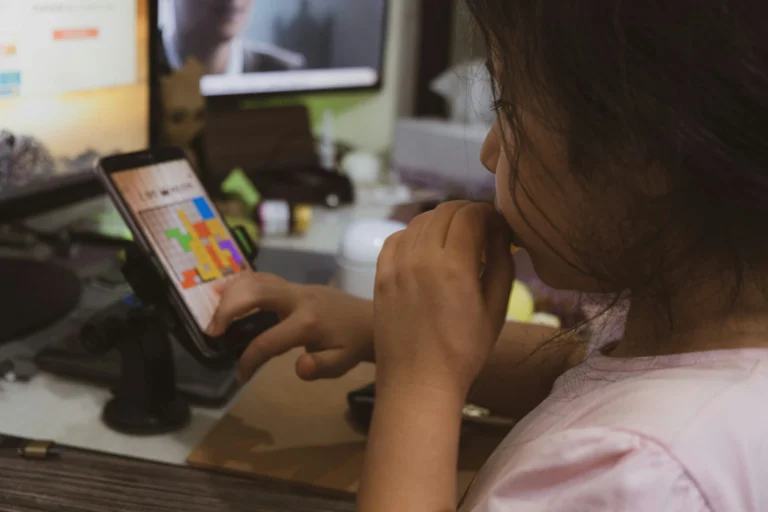 Young girl with dark hair playing a colorful block puzzle game on a smartphone.