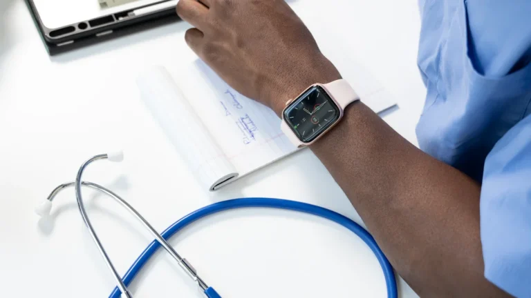A close-up of a health worker's hand resting on a notepad with a stethoscope and digital tablet.