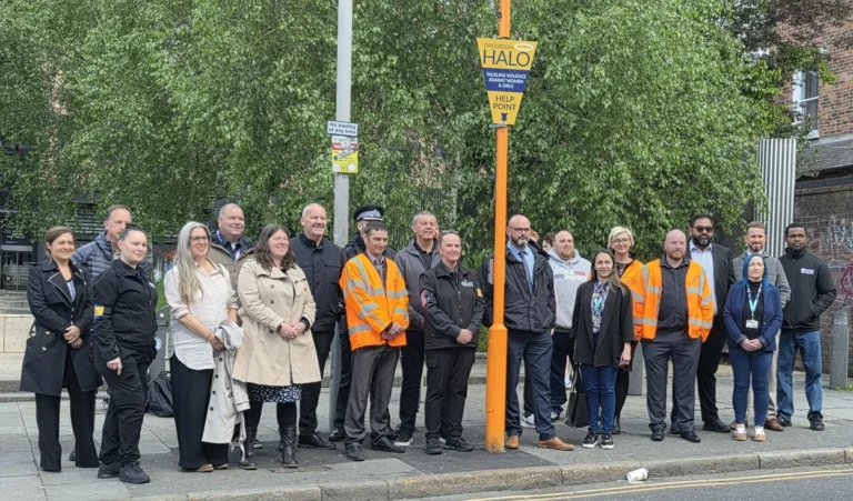 A group of people stand next to an orange Operation Halo help point pole outdoors.