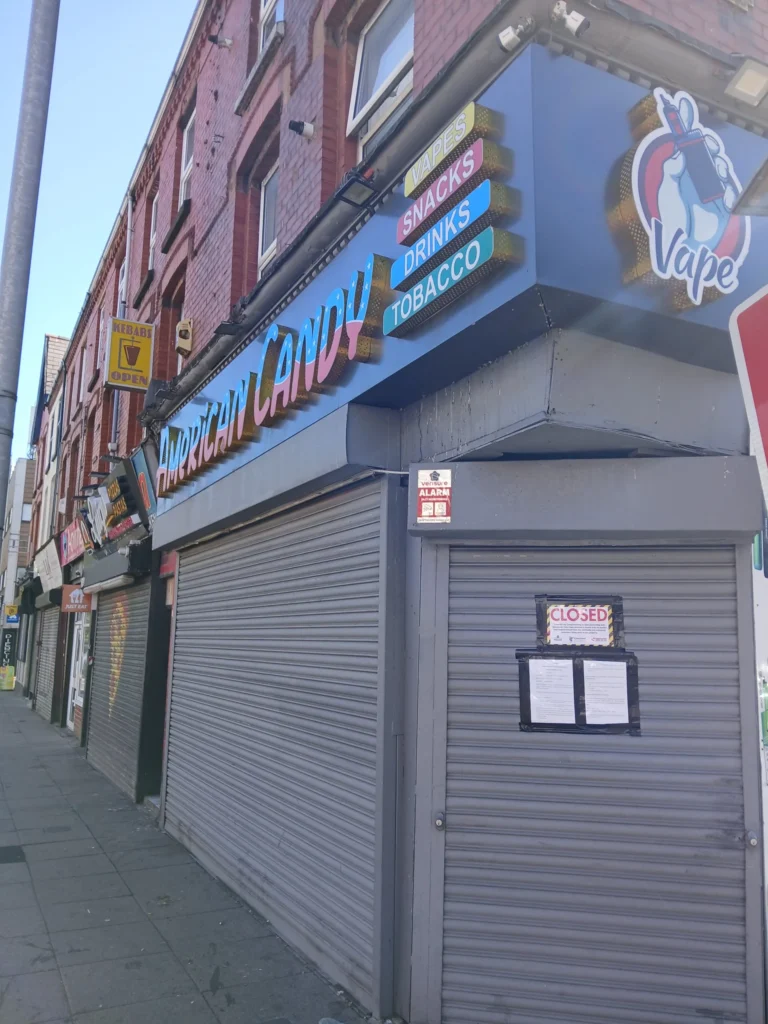 American Candy and Vape shopfront with grey security shutters down and a closure notice attached.