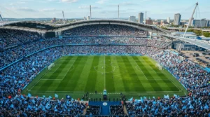 Wide-angle view of a crowded football stadium with fans in light blue watching a match.