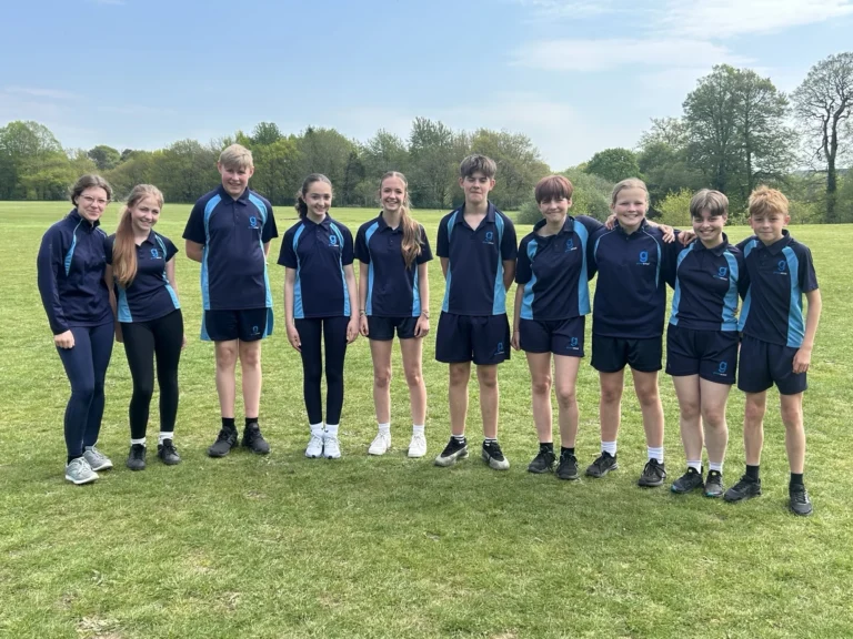 Ten students in matching blue sports kits stand in a line on an open field.