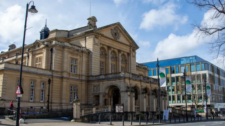 A wide view of a grand historic stone civic building with classical columns under a blue sky.