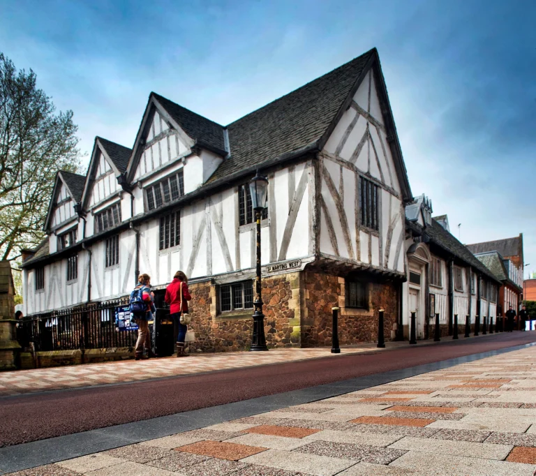 Historic timber-framed building on a street corner with people walking past on the sidewalk.