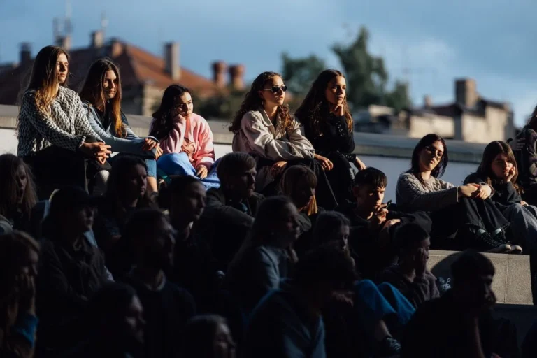 Young people sitting on tiered outdoor steps in sunlight with buildings in the background.