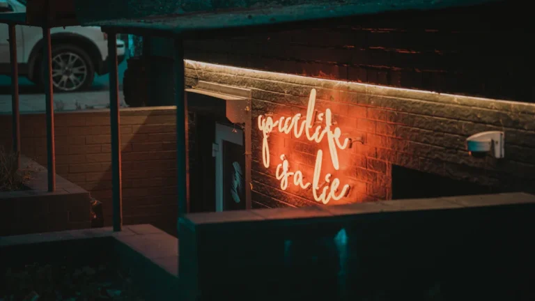 A neon sign in a dark, underground entryway that reads 'your life is a lie,' used as a metaphor for the deception in human trafficking.