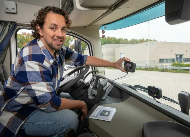 A man in a plaid shirt holding a small electronic device against a truck's front windshield.