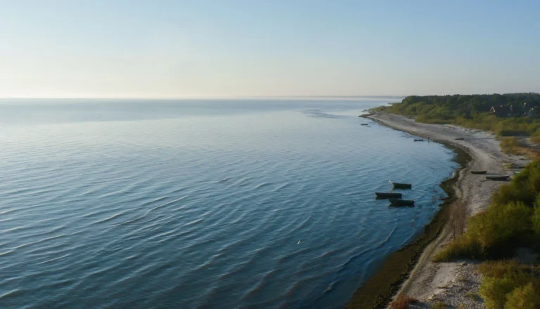 High-angle view of a calm sea meeting a sandy beach with small wooden boats anchored nearby.