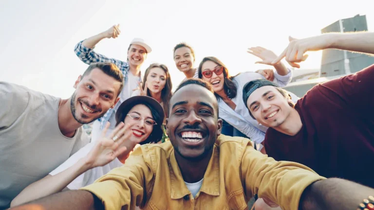 A smiling, diverse group of young adults from various ethnic backgrounds taking a group selfie outdoors, symbolizing community unity.