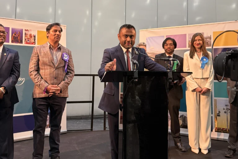 A man in a suit speaks at a podium with several candidates standing behind him.