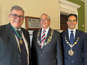 Three men in suits and ceremonial chains stand before a North Yorkshire Council commemorative plaque.