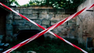 Red and white hazard tape forming a cross over a stone wall entrance, symbolizing a legal closure order.