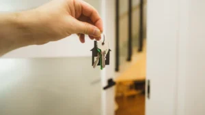 A close-up shot of a hand holding a set of keys with a house-shaped keychain in a bright home interior.
