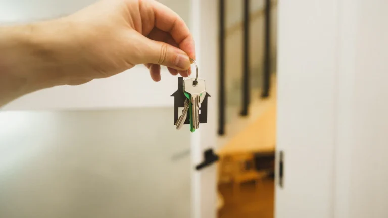 A close-up shot of a hand holding a set of keys with a house-shaped keychain in a bright home interior.