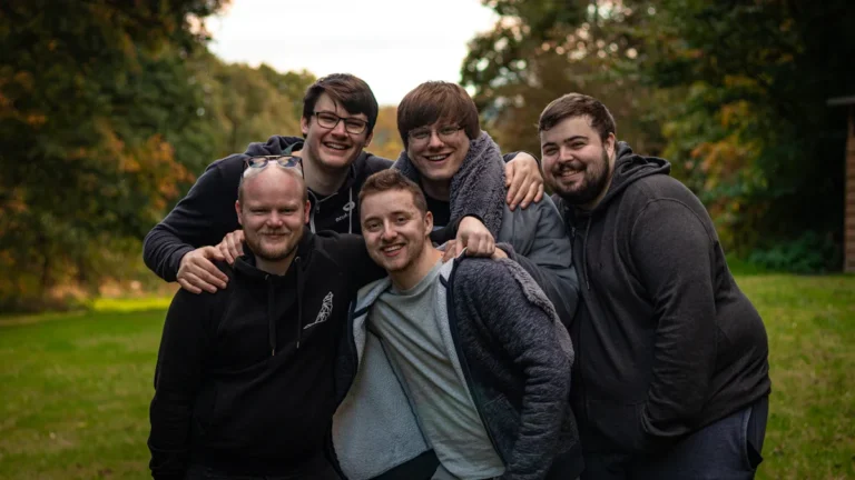 A group of five men smiling and huddling together in a park, showcasing friendship and support.