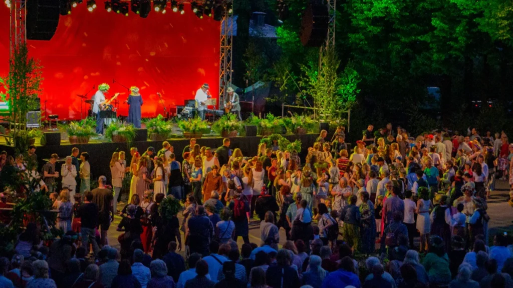 A large crowd gathered in front of an outdoor stage for a summer festival in a park in Latvia.