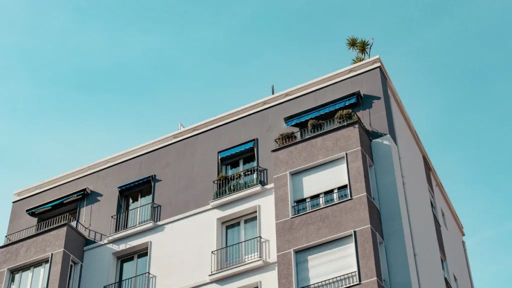 A modern multi-story apartment building with white and grey facades under a clear blue sky.